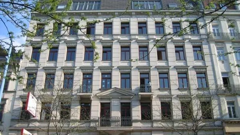 Klassisches Mehrfamilienhaus mit vielen Fenstern und Balkonen in einer städtischen Umgebung.