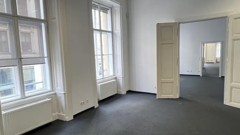 Geräumiges Büro mit großen Fenstern, Teppichboden und Zugang zu weiteren Räumen, ideal für flexible Arbeitsbereiche.