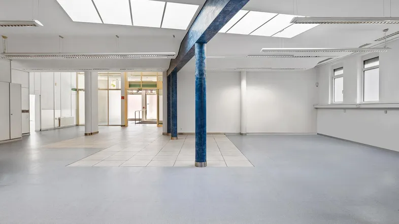 Geräumiger, heller Gewerberaum mit hohen Decken, Oberlichtern und markanten blauen Säulen, ideal für flexible Nutzung.