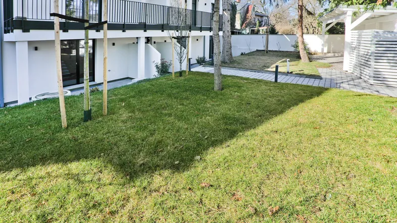 Moderne Wohnanlage mit weißer Fassade, Balkonen und gepflegter Rasenfläche im Außenbereich.