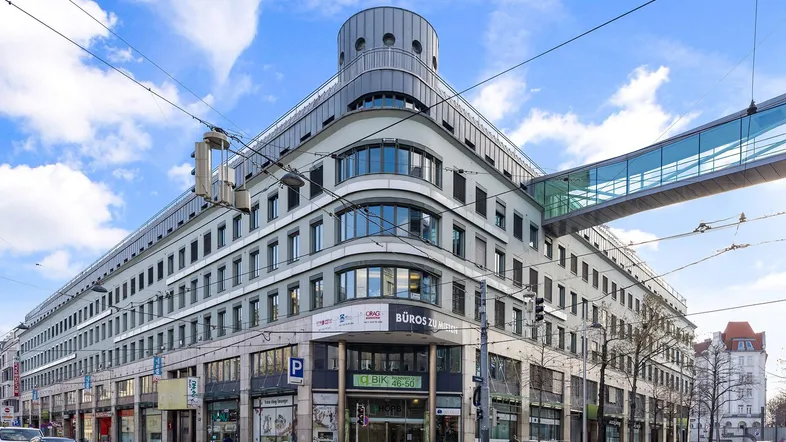 Modernes Bürogebäude an einer belebten Straße mit markanter Architektur und einer Fußgängerbrücke.
