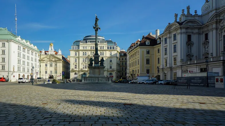 Historischer Stadtplatz mit Kopfsteinpflaster, umgeben von klassischen Gebäuden unter blauem Himmel.