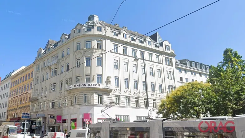 Historisches Gebäude mit klassischer Architektur, Straßenbahn und belebter Umgebung in der Stadt.