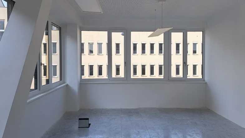 Heller, leerer Raum mit großen Fenstern, die viel Tageslicht hereinlassen, und einem hellen Fliesenboden.