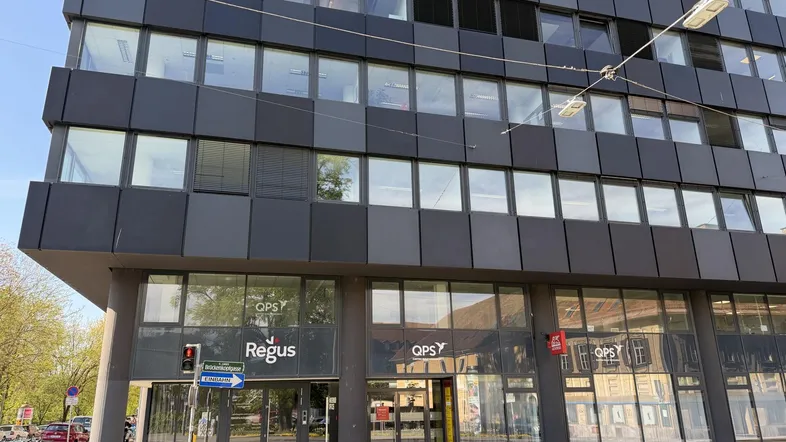 Modernes Bürogebäude mit dunkler Fassade und großen Fenstern, im Erdgeschoss befinden sich Geschäftsräume.