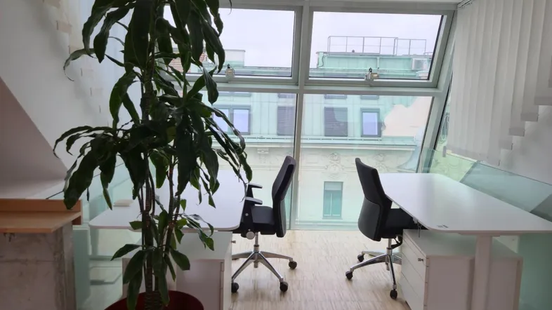 Helles Büro im Dachgeschoss mit großen Fenstern, modernen Arbeitsplätzen und Blick auf die Stadt.