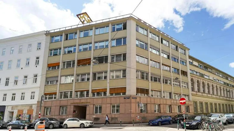Mehrstöckiges Geschäftsgebäude an einer Straßenecke mit vielen Fenstern und parkenden Autos.