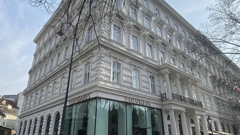 Klassisches Gebäude mit aufwendiger Fassade, großen Fenstern und Geschäftsräumen im Erdgeschoss.