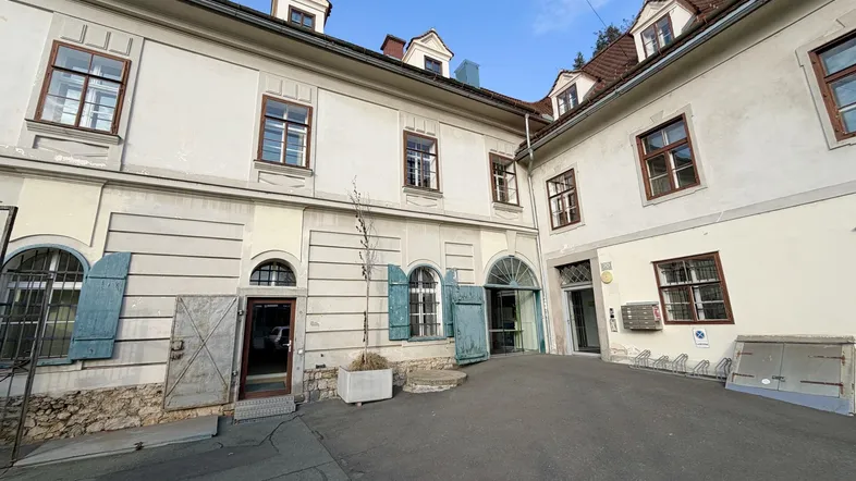 Historisches Gebäude mit heller Fassade, vielen Fenstern und einem gepflasterten Innenhof.