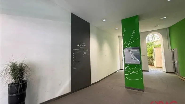 Heller Eingangsbereich mit Informationssäule, Pflanzen und Zugang zu einem Innenhof.