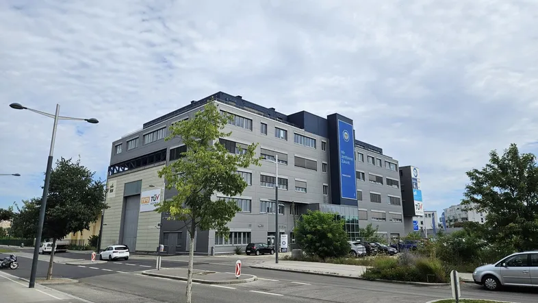 Großes modernes Bürogebäude mit mehreren Etagen und Parkplätzen an einer Straße.