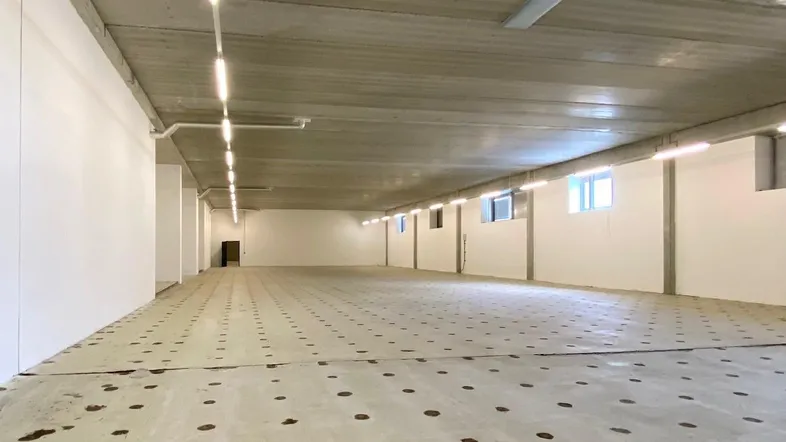 Großer, leerer Gewerberaum mit Betonboden und -decke, weißen Wänden und effizienter Beleuchtung.