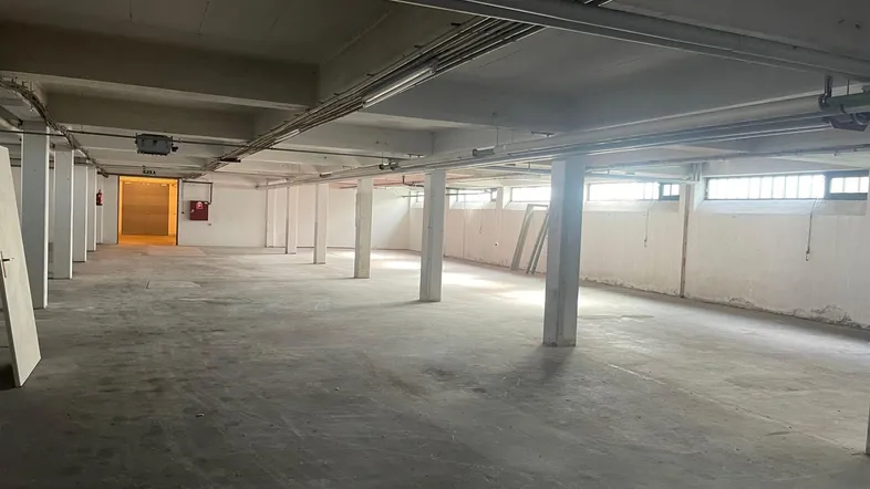 Großer, leerer Lagerraum mit Betonboden, vielen Säulen und sichtbaren Leitungen an der Decke.