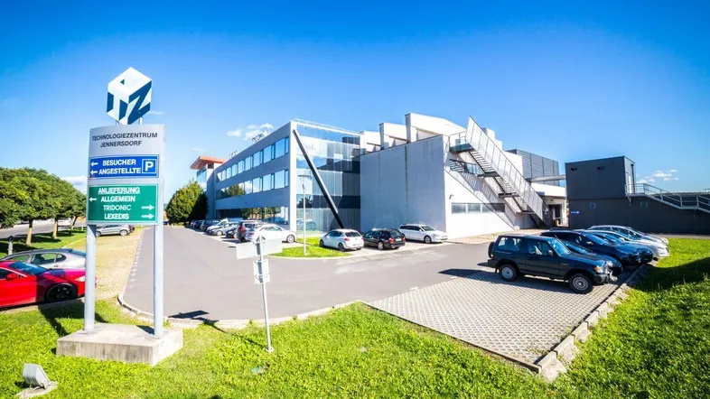 Modernes Technologiezentrum mit Glasfassade und großem Parkplatz unter blauem Himmel.