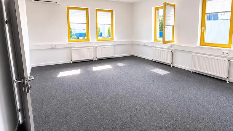Helles und geräumiges Büro mit grauem Teppichboden, Klimaanlage und gelben Fensterrahmen.
