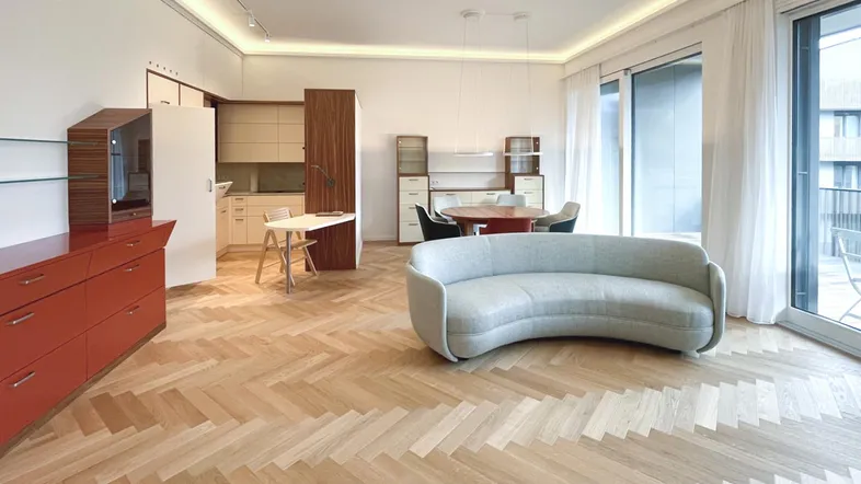 Helles, offenes Wohn-Esszimmer mit Fischgrätparkett, moderner Einrichtung und Zugang zum Balkon.