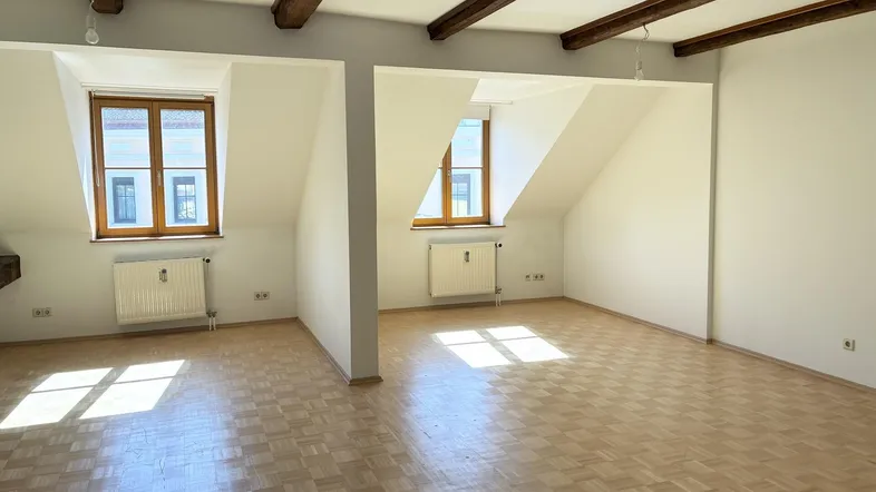 Heller Dachgeschossraum mit sichtbaren Holzbalken, Schrägen und Parkettboden.