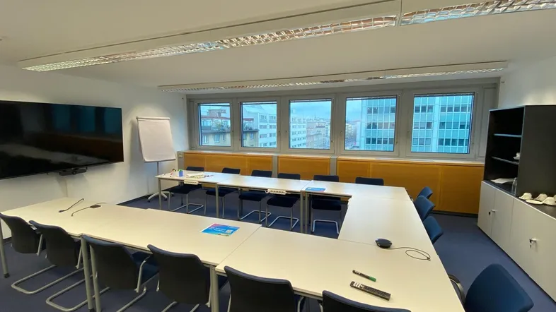 Geräumiger Konferenzraum mit U-förmigem Tisch, großem Bildschirm und Blick auf die Stadt.