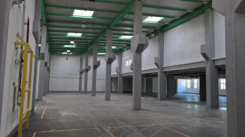 Große, leere Lagerhalle mit hohen Decken, vielen Säulen und Oberlichtern für natürliches Licht.