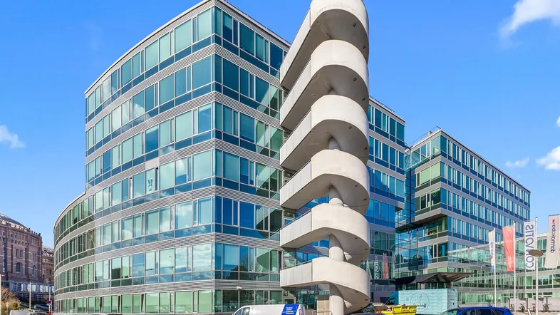 Modernes Bürogebäude mit Glasfassade und auffälliger Außentreppe unter blauem Himmel.