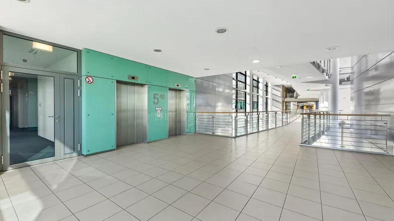 Helle, moderne Lobby mit Fliesenboden, Aufzügen und großen Fenstern in einem Bürogebäude.