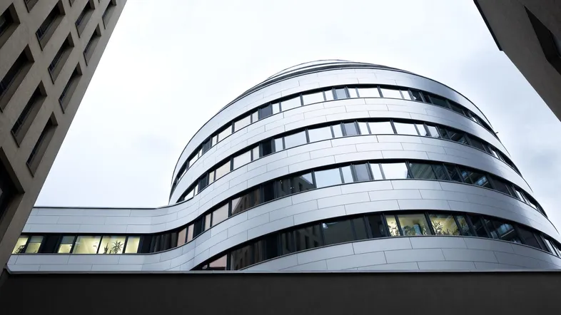 Modernes Bürogebäude mit geschwungener Fassade und vielen Fenstern, von unten fotografiert.