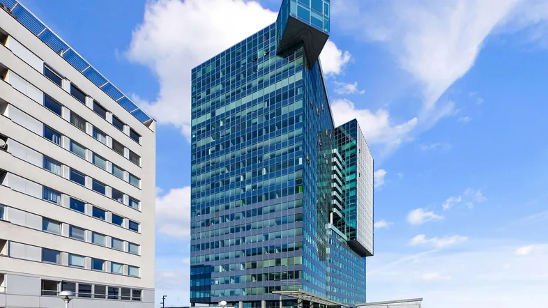 Modernes Hochhaus mit markanter Glasfassade und einzigartiger Architektur unter blauem Himmel.
