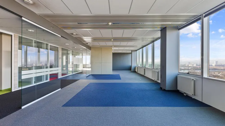 Großes, offenes Büro mit Teppichboden, Glaswänden und weitem Ausblick durch die Fenster.