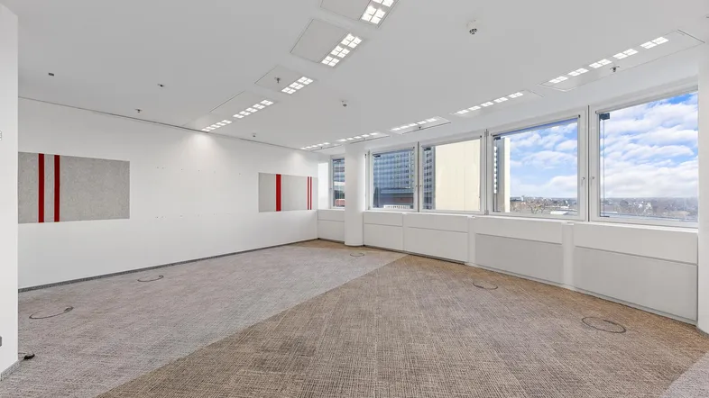Geräumiges, modernes Büro mit großen Fenstern, Teppichboden und Blick auf die Stadt, ideal für Erstbezug.