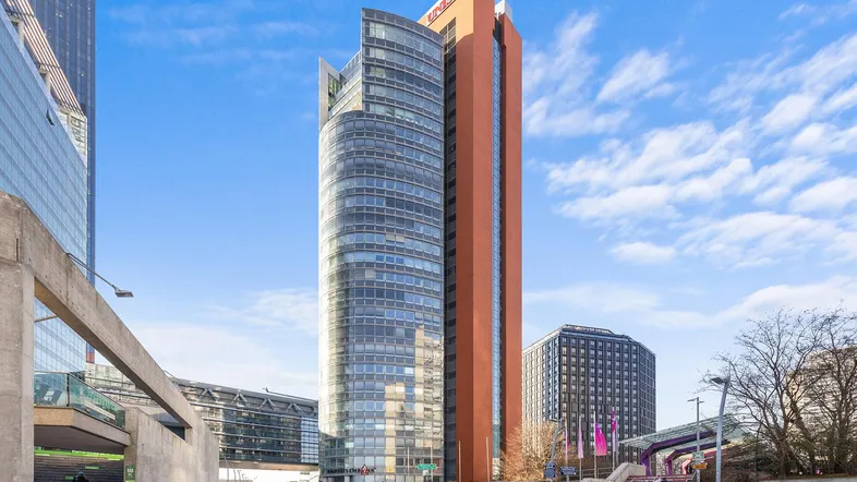 Moderne Hochhäuser mit Glasfassaden und einer belebten Plaza unter blauem Himmel.