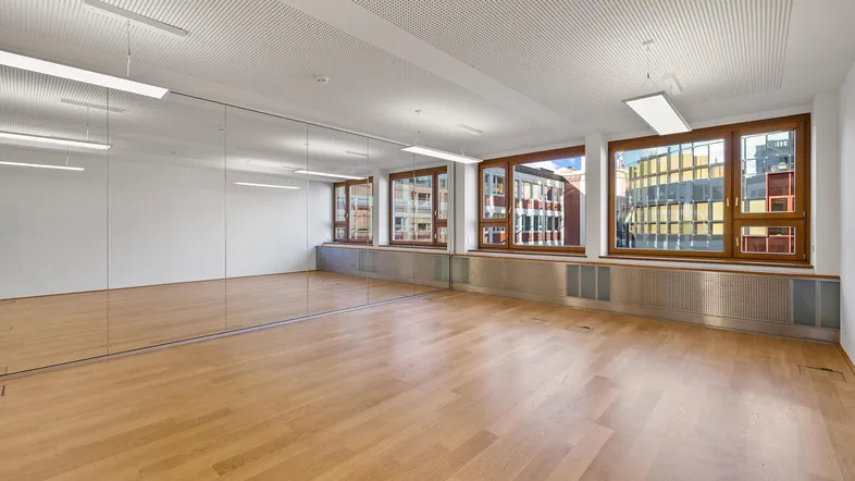 Geräumiger Büroraum mit Holzboden, großer Spiegelfront und Blick auf die Stadt durch mehrere Fenster.
