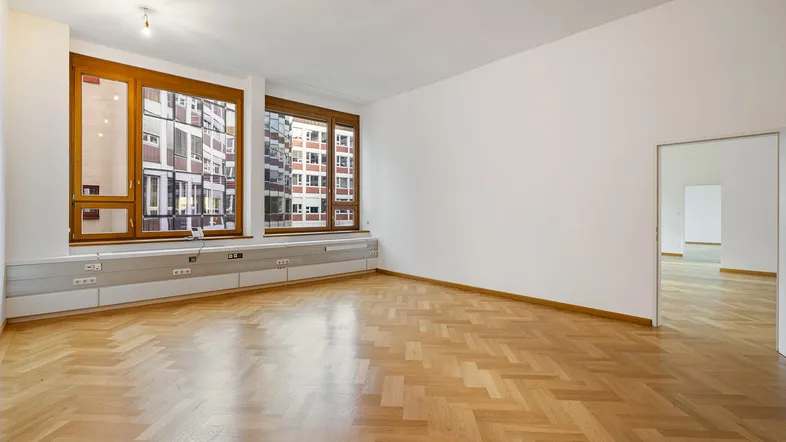 Heller Büroraum mit Fischgrätparkett und großen Holzfenstern, die viel Tageslicht hereinlassen.