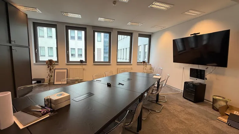 Großer Konferenzraum mit langem Tisch, modernen Stühlen und Wandfernseher für Präsentationen.