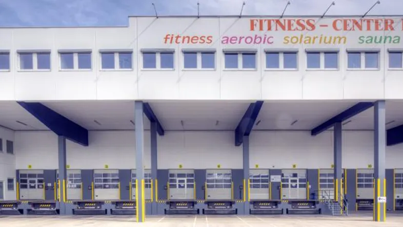 Modernes Geschäftsgebäude mit mehreren Laderampen und einem Fitness-Center-Schild im oberen Bereich.