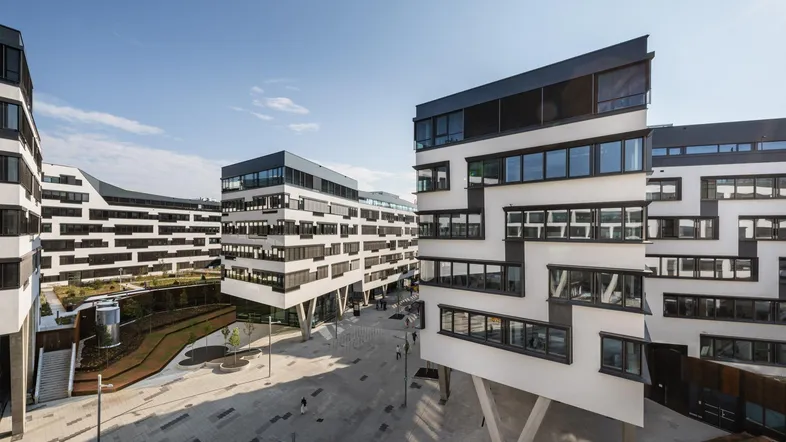 Moderne Bürogebäude mit markanter Architektur und gepflastertem Vorplatz unter blauem Himmel.
