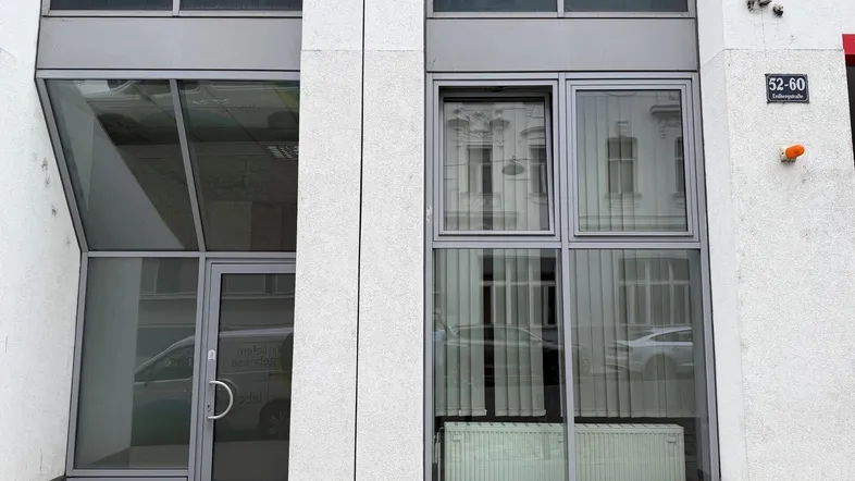 Eingangsbereich eines modernen Geschäftsgebäudes mit großer Glasfassade und sichtbarer Überwachungskamera.