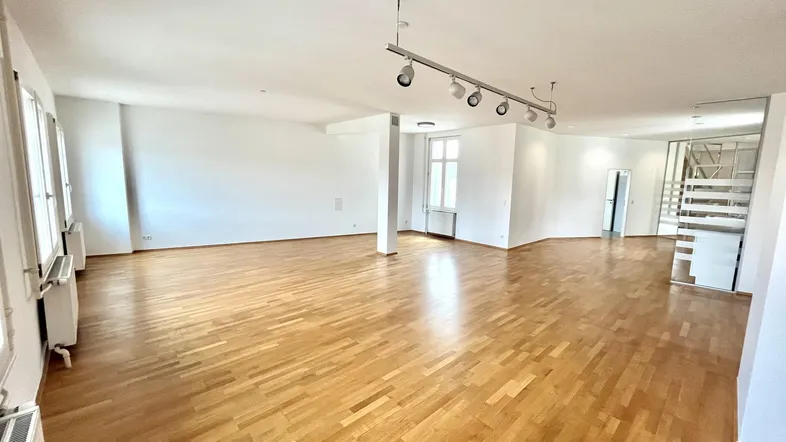 Geräumiges, helles Wohnzimmer mit Parkettboden und großen Fenstern, das viel natürliches Licht bietet.