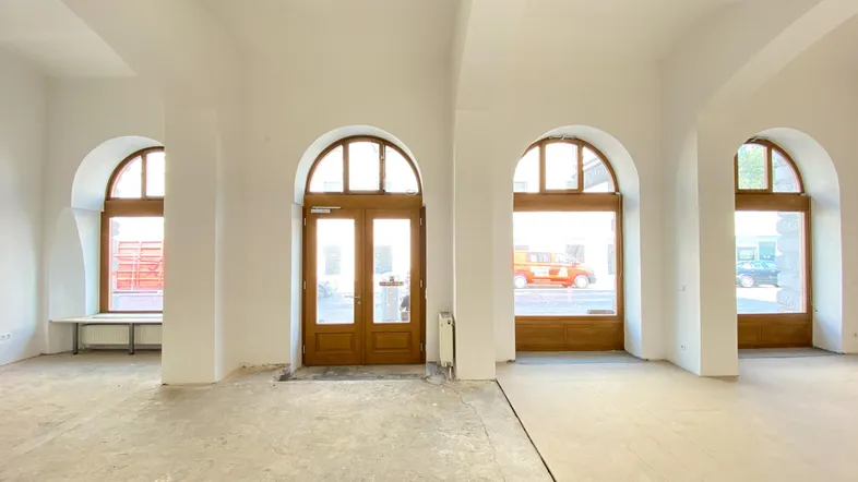 Großer, leerer Raum mit hohen Gewölbedecken, großen Rundbogenfenstern und einer Holztür, bereit für den Ausbau.
