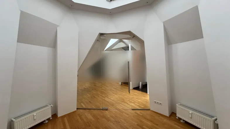 Heller Raum mit einzigartiger Deckenarchitektur, Holzboden und einer modernen Milchglastür.