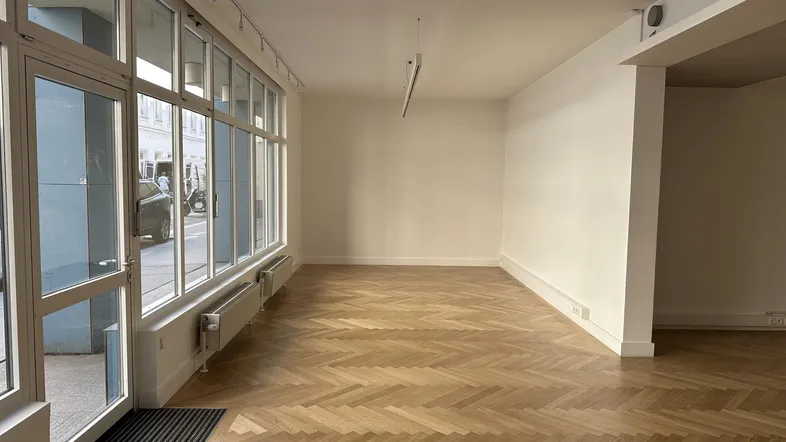 Geräumiger, heller Büroraum mit Fischgrätparkett und großen Fenstern zur Straße.