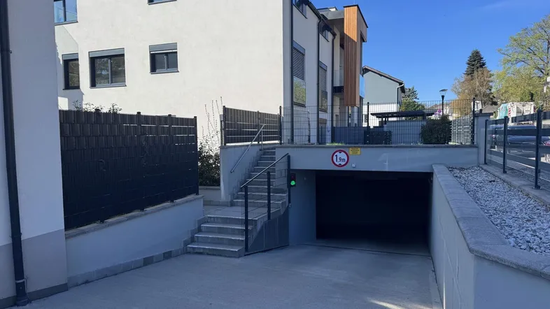 Eingang zur Tiefgarage eines modernen Wohngebäudes mit Rampe und Treppe.