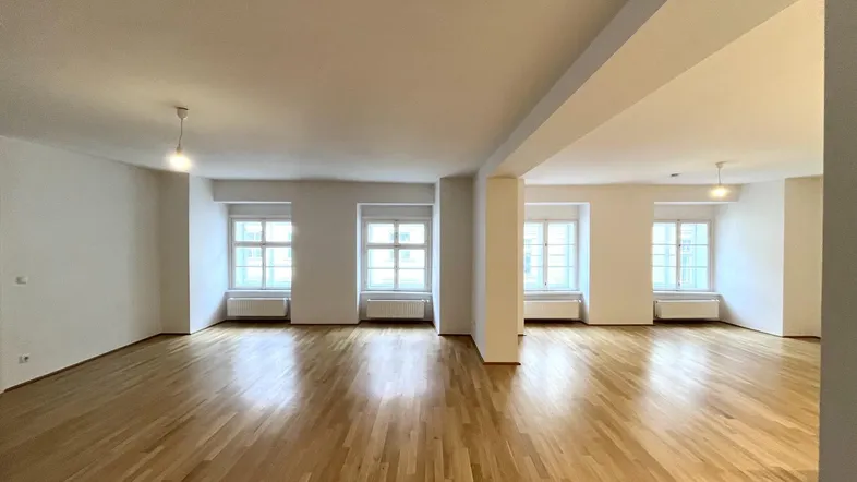 Helles, leeres Wohnzimmer mit Parkettboden und mehreren Fenstern, bereit zur individuellen Gestaltung.