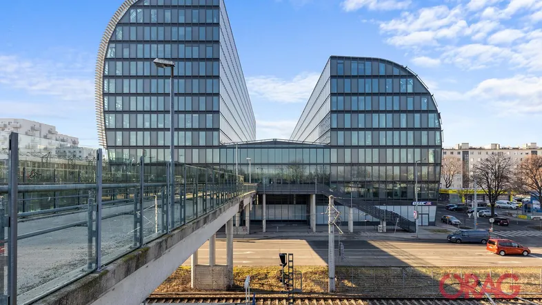 Modernes Bürogebäude mit geschwungener Glasfassade und Blick auf die Stadt und Bahngleise.