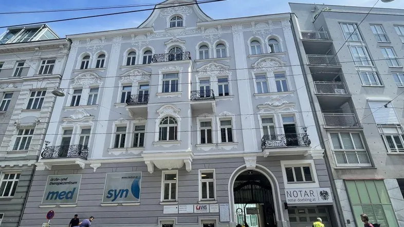 Historisches Gebäude mit klassischer Fassade, vielen Fenstern und Geschäftsräumen im Erdgeschoss.