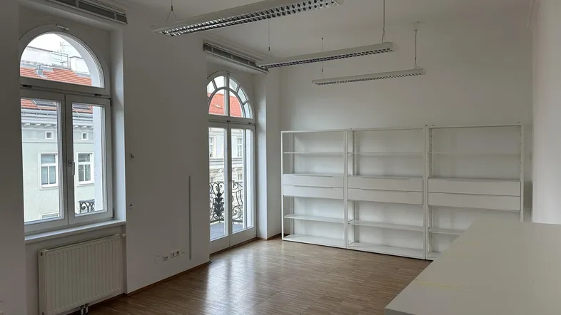 Helles Büro mit hohen Bogenfenstern, Holzboden und weißen Regalen, ideal für Arbeitsbereiche.