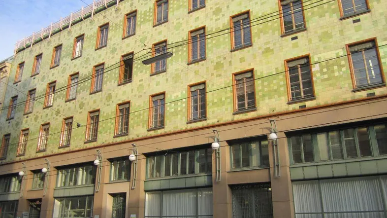 Grünes Gebäude mit vielen Fenstern und einer interessanten Fassadenstruktur in einer städtischen Umgebung.