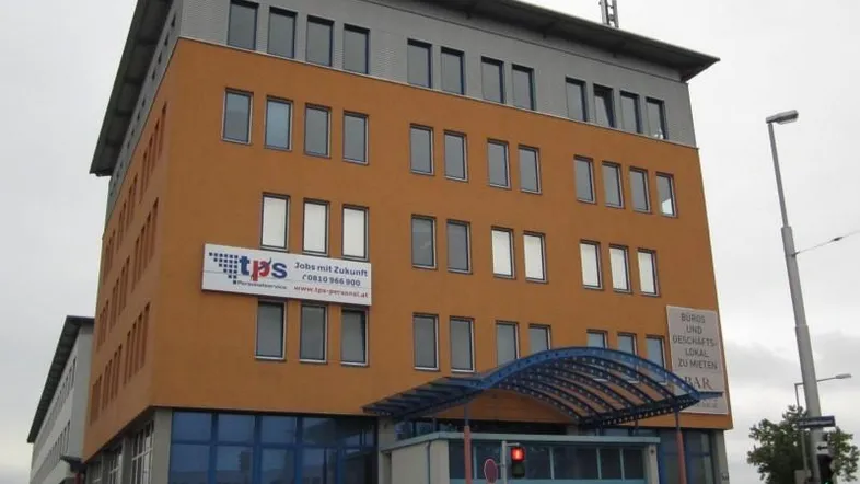 Modernes Bürogebäude mit orangefarbener Fassade, blauer Glasfront und mehreren Etagen.