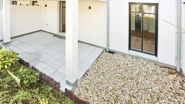 Helle, gepflasterte Terrasse mit Zugang zum Innenbereich und Kiesbeet.