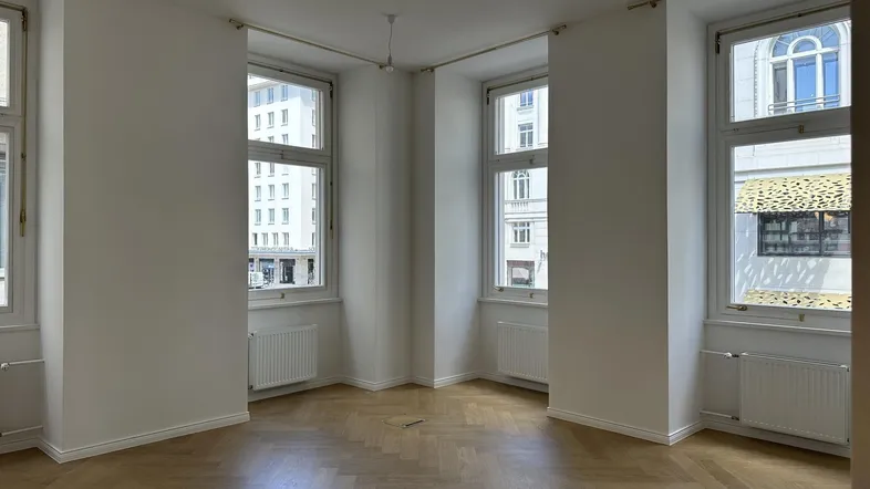 Heller Raum mit Fischgrätparkett, hohen Fenstern und weiß gestrichenen Wänden, ideal für Wohn- oder Büronutzung.