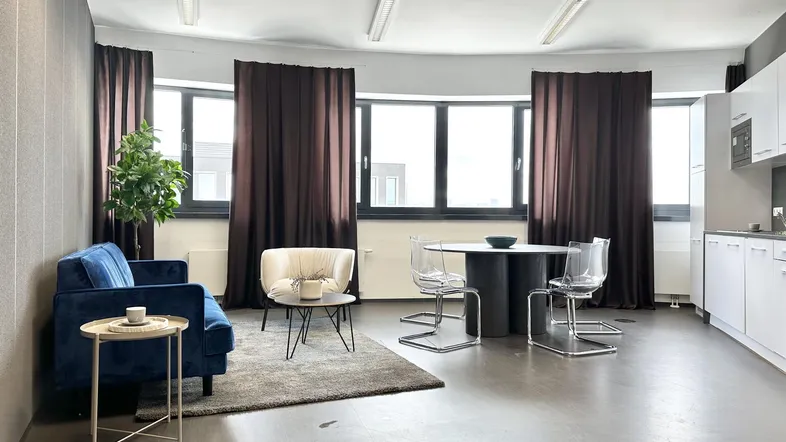 Moderner Büroraum mit Sitzgelegenheiten, Esstisch und integrierter Küchenzeile, ideal für flexible Arbeitsbereiche.